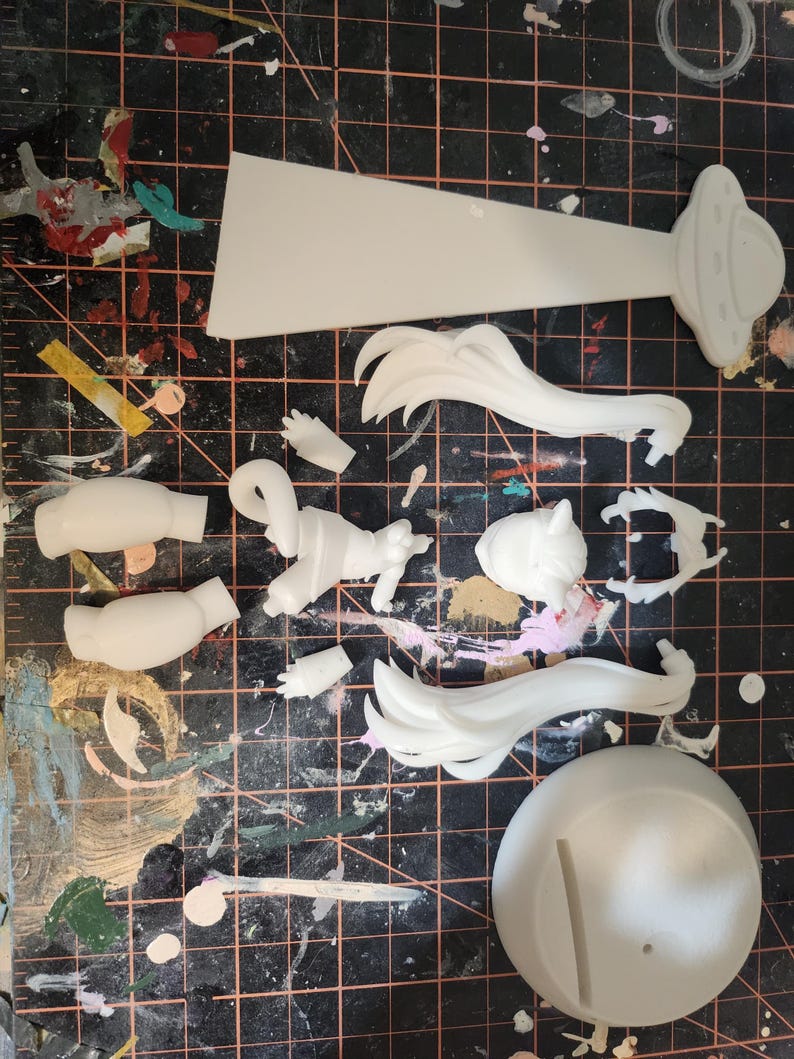 May include: White plastic model kit pieces for assembling a figure. The pieces include a head, arms, legs, hair, a base, and a flying saucer.