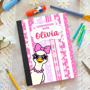 May include: A composition book with a pink and white striped cover featuring a white duck wearing a pink bow and star-shaped sunglasses. The text reads Composition Book and Olivia. The cover has floral and star patterns with a black spine.