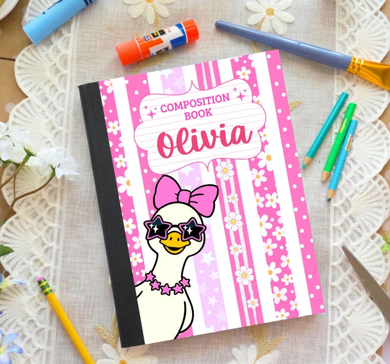 May include: A composition book with a pink and white striped cover featuring a white duck wearing a pink bow and star-shaped sunglasses. The text reads Composition Book and Olivia. The cover has floral and star patterns with a black spine.