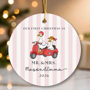 Puede incluir: Un adorno de cerámica redondo con un fondo de rayas verticales rosas y blancas. Presenta un gráfico de dos patos blancos montando un scooter rojo con sidecar. El texto dice: OUR FIRST CHRISTMAS AS MR. & MRS. Mason & Emma 2026.