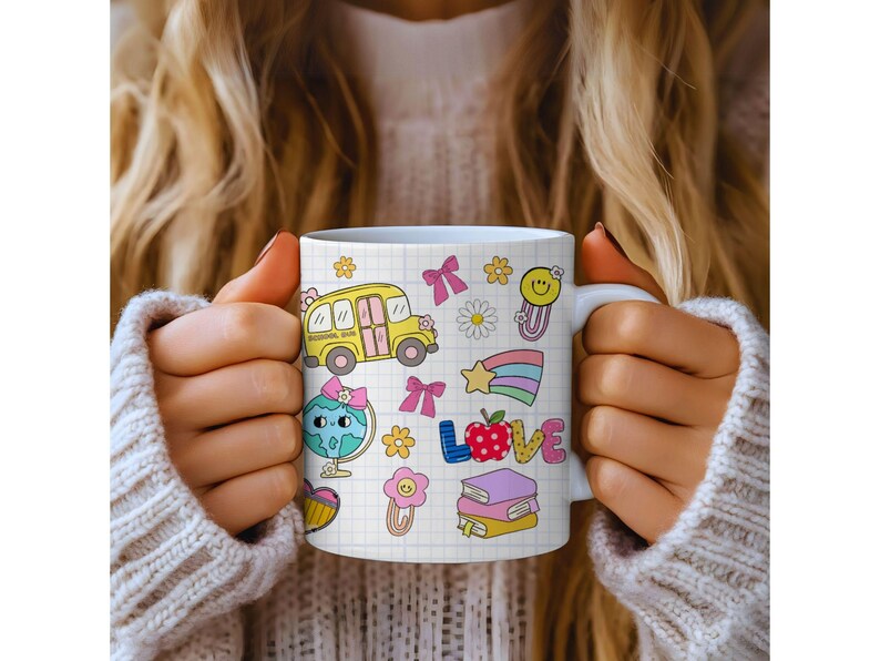 May include: White ceramic mug featuring colorful school-themed illustrations, including a yellow school bus, a globe, and the word "LOVE". The mug has a grid pattern background and is held by a person wearing a white sweater.