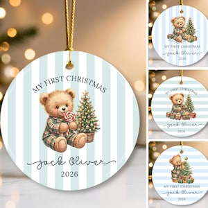 Puede incluir: Un adorno navideño redondo de cerámica con fondo de rayas azul claro y blanco. El diseño incluye un oso de peluche marrón en pijama de cuadros sosteniendo una piruleta junto a un árbol de Navidad decorado. Texto: My First Christmas, Jack Oliver, 2026.