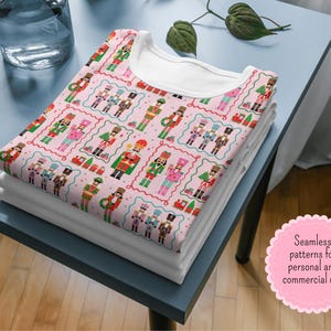 May include: A stack of folded white t-shirts with a patterned t-shirt on top. The top shirt features a repeating design of colorful nutcracker figures on a pink background. The design includes text that reads "Seamless patterns for personal and commercial use."