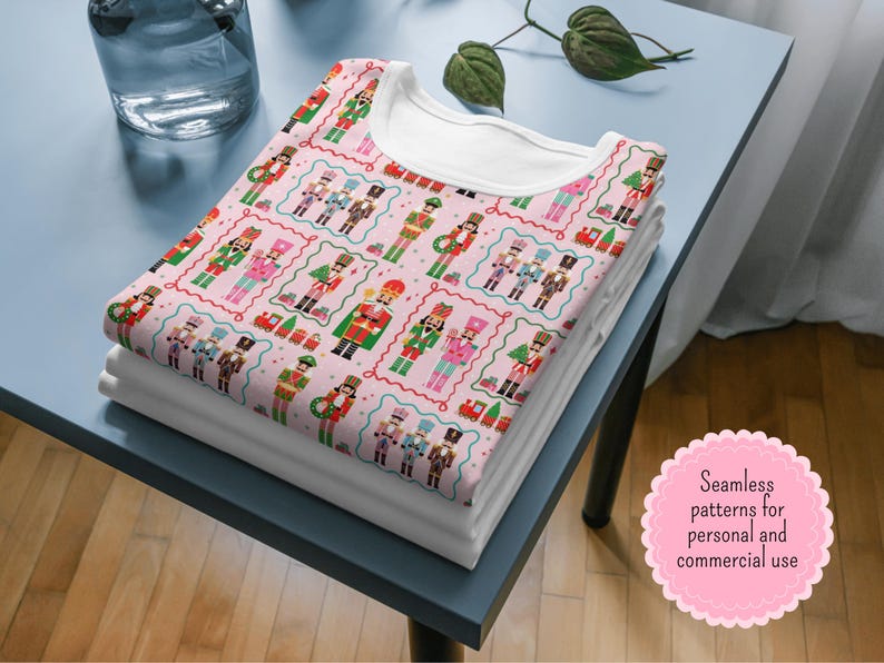 May include: A stack of folded white t-shirts with a patterned t-shirt on top. The top shirt features a repeating design of colorful nutcracker figures on a pink background. The design includes text that reads "Seamless patterns for personal and commercial use."