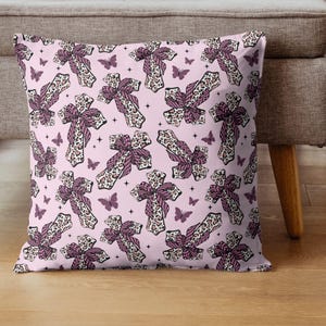 May include: A cushion featuring a repeating pattern of crosses and butterflies on a pale pink backdrop. The crosses have a leopard print design with a purple bow. The butterflies are purple.