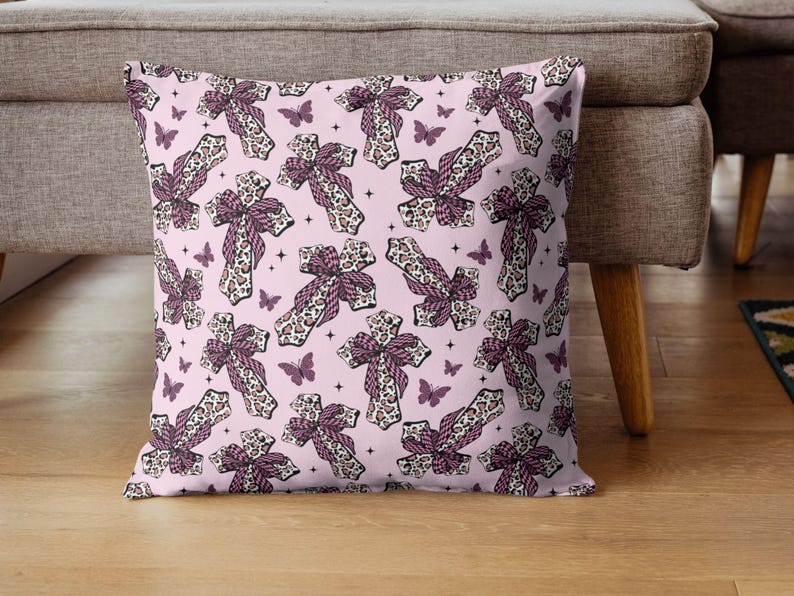 May include: A cushion featuring a repeating pattern of crosses and butterflies on a pale pink backdrop. The crosses have a leopard print design with a purple bow. The butterflies are purple.