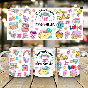 May include: White ceramic mug with a colorful teacher-themed design. The design includes rainbows, school buses, pencils, and the text "Best teacher ever Mrs. Smith". The mug is on a wooden surface.