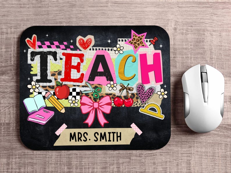 May include: Black rectangular mousepad with the word "TEACH" in colorful letters and school-themed graphics. Includes a pink bow, apple, pencil, and the name "MRS. SMITH". A white computer mouse is to the right.