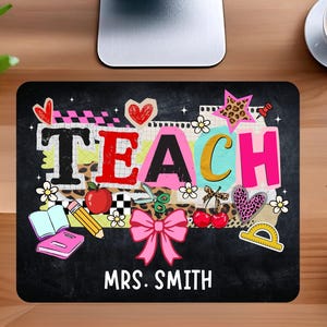 May include: Black rectangular mousepad with the word "TEACH" in colorful letters, decorated with school-themed graphics like hearts, apples, and a pink bow. The name "MRS. SMITH" is printed below.