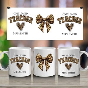 Puede incluir: Tazas de cerámica blanca con un diseño "ONE LOVED TEACHER" en estampado de leopardo, un corazón con estampado de leopardo y el nombre "MRS. SMITH". También se muestra un lazo a juego con estampado de leopardo. El diseño se repite en una impresión colgante.