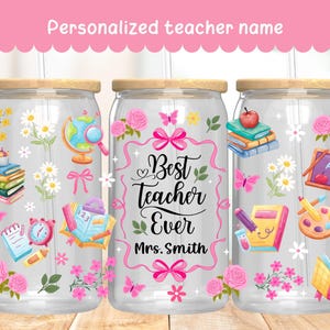 Puede incluir: Vaso de vidrio transparente con tapa y pajita de madera, decorado con ilustraciones escolares. El vaso presenta el texto "Best Teacher Ever" y "Mrs. Smith", junto con flores rosas, mariposas y útiles escolares.