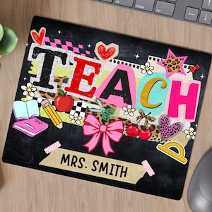 May include: Black mousepad with the word "TEACH" in colorful letters, decorated with school-themed graphics like an apple, pencil, and bow. The name "MRS. SMITH" is printed below. A succulent, notepad, and mouse are also visible.