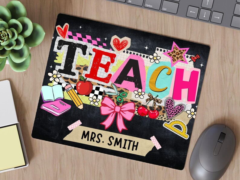 May include: Black mousepad with the word "TEACH" in colorful letters, decorated with school-themed graphics like an apple, pencil, and bow. The name "MRS. SMITH" is printed below. A succulent, notepad, and mouse are also visible.