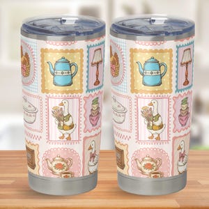 May include: Two stainless steel tumblers with clear plastic lids, featuring a repeating pattern of rectangular frames containing illustrations of blue teapots, geese, floral teapots, lamps, and stacks of teacups on a light pink background.