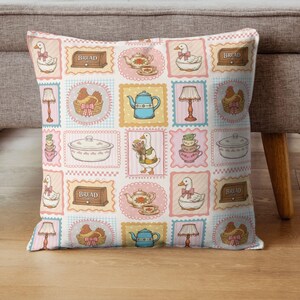 May include: A square throw pillow featuring a repeating grid pattern of illustrations including white geese with pink bows, blue teapots, brown bread boxes labeled BREAD, lamps, chickens in baskets, stacked teacups, and covered casserole dishes.