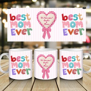 Puede incluir: Taza de cerámica blanca con el texto "best MOM ever" en letras de patchwork coloridas. También presenta un corazón decorativo con un lazo rosa y el texto "We love you! Amelia & Oliver". Se muestra un póster a juego.