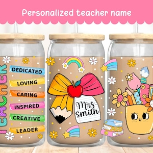 Może przedstawiać: Trzy szklane kubki z bambusowymi pokrywkami i słomkami, z motywami dla nauczycieli. Jeden kubek ma słowo "TEACHER" pionowo i przymiotniki takie jak "DEDICATED" i "LOVING". Inny ma ołówek, kokardę i jabłko z napisem "Mrs. Smith". Trzeci ma uśmiechniętą doniczkę z przyborami szkolnymi. U góry znajduje się tekst "Personalized teacher name".
