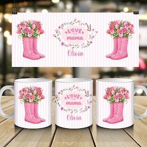 Puede incluir: Taza de cerámica blanca con un diseño de rayas rosas y blancas. La taza presenta una ilustración de acuarela de botas de agua rosas llenas de tulipanes rosas y rojos. También se muestran las palabras "Love You Mama" y el nombre "Olivia".
