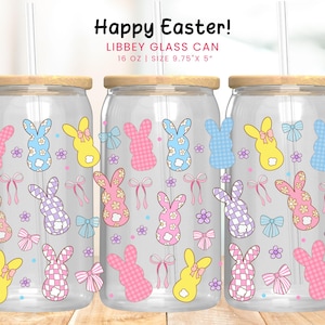 Puede incluir: Tres latas de vidrio transparente con tapas de madera y pajitas, decoradas con coloridos diseños de conejitos de Pascua. El texto "Happy Easter!" está en la parte superior. Cada lata es de 16 oz y mide 24,77 cm x 12,7 cm.