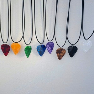 Può includere: Nove plettri per chitarra su cordini neri, ogni plettro è di un colore diverso: rosso, arancione, verde, blu, viola, marrone, nero, bianco e trasparente.