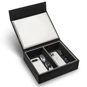Puede incluir: Caja de almacenamiento de cuero negro con interior blanco y compartimentos divididos. La caja contiene un teléfono inteligente blanco, una llave de coche plateada y un reloj inteligente. El texto "BLOCK BOX" es visible en la parte inferior derecha.