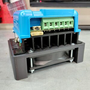 May include: A blue and black electronic component with a green terminal block and a 25-amp fuse. The device has a black heat sink and a fan, mounted on a gray surface.