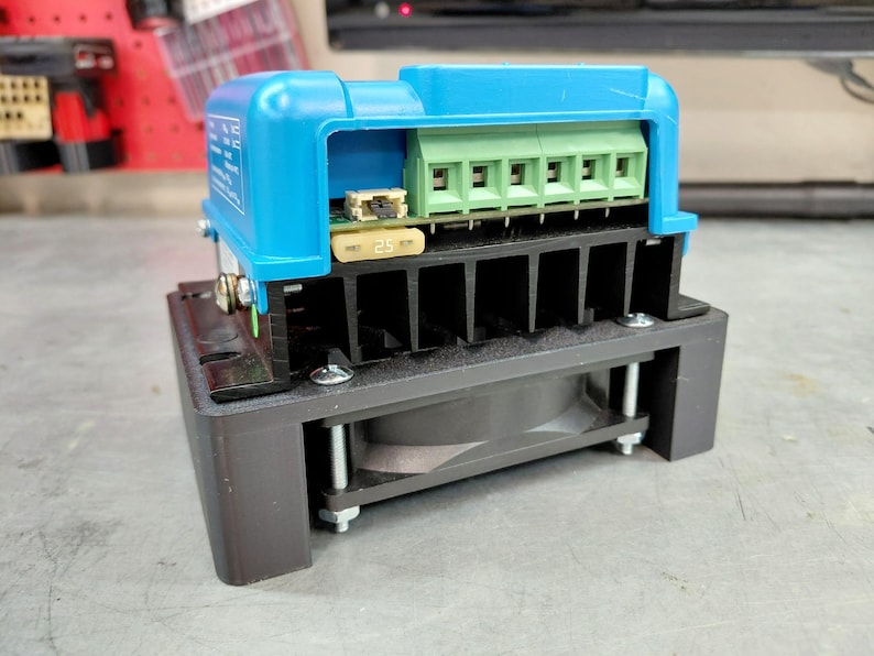 May include: A blue and black electronic component with a green terminal block and a 25-amp fuse. The device has a black heat sink and a fan, mounted on a gray surface.