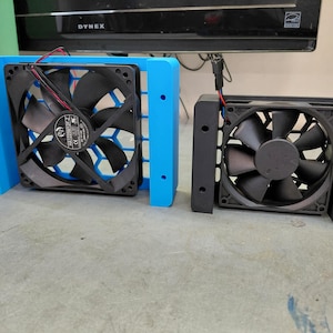 May include: Two computer fans, one blue and one black, are displayed side-by-side. The blue fan has a honeycomb-patterned grill. Both fans have black blades and are mounted in rectangular frames. The fans have red and black wires.
