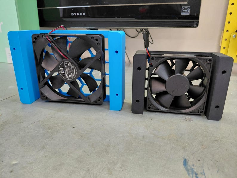 May include: Two computer fans, one blue and one black, are displayed side-by-side. The blue fan has a honeycomb-patterned grill. Both fans have black blades and are mounted in rectangular frames. The fans have red and black wires.
