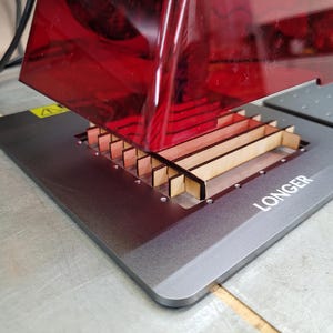 Może przedstawiać: Czerwona drukarka 3D żywiczna z drewnianą platformą i nadrukiem "LONGER" na platformie.