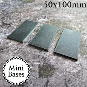 May include: Three rectangular, dark grey, textured plastic bases for miniature figures. The bases are 50mm by 100mm. The text "Mini Bases" is printed on a black and white chequered circle.