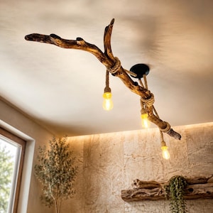May include: A ceiling light fitting featuring a large, natural brown wooden branch suspended from a black circular mount. Three light bulbs hang from the branch, each wrapped in thick, tan-coloured rope, emitting a warm, soft yellow glow.
