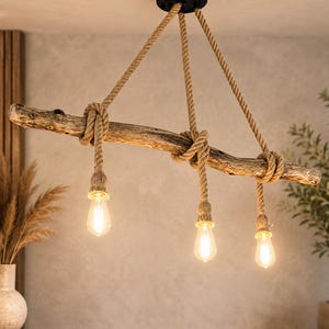 May include: A hanging light fitting featuring a natural driftwood branch suspended by thick, tan-coloured jute ropes. Three light bulbs hang from the branch, each encased in a matching rope-wrapped socket, emitting a warm, soft glow.