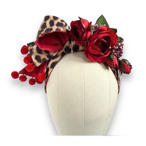 May include: A red and leopard print headband with red pom-poms and a red rose flower accent.