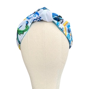 May include: A white and blue patterned headband with a knotted design. The headband features a blue and white floral pattern with yellow accents.
