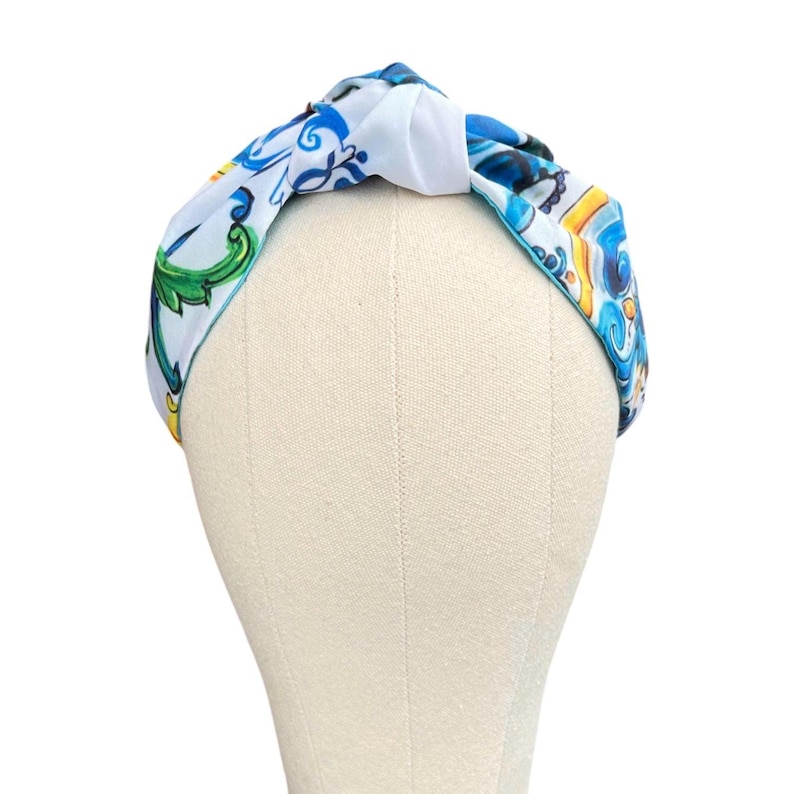 May include: A white and blue patterned headband with a knotted design. The headband features a blue and white floral pattern with yellow accents.
