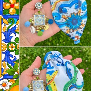 May include: A pair of blue and white patterned fabric headbands with a gold and blue tile-inspired earring with green and white accents.