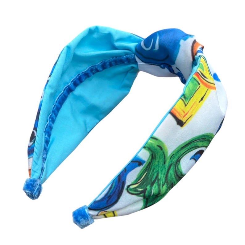 May include: A blue and white headband with a knotted design. The headband is decorated with a colorful pattern of green, yellow, and blue.