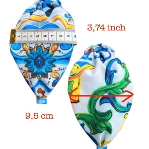 May include: Two fabric pouches with a colorful floral pattern. The pouch on the left is measured with a tape measure, showing a width of 9.5 cm. The pouch on the right is measured with a red line, showing a width of 3.74 inches.