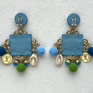 May include: A pair of blue and gold statement earrings with a square blue leather center, gold accents, and blue, green, and white beads.