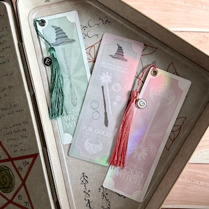 May include: Three decorative bookmarks with tassels and charms. The bookmarks feature illustrations of witch hats, wands, and brooms. One bookmark has the text "THE WICKED WITCH", another says "FOR GOOD", and the last says "THE GOOD WITCH".