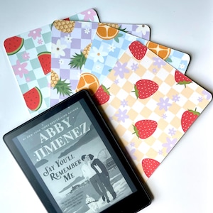 May include: An e-reader displaying the book "Say You'll Remember Me" by Abby Jimenez, with colorful fruit-patterned bookmarks. The bookmarks feature watermelon, pineapple, orange, and strawberry designs on checkered backgrounds.