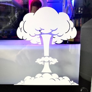 May include: A white silhouette of a mushroom cloud explosion on a clear glass surface. The background is a blurred image of a computer case with colorful lights.