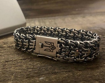 May include: A silver chain bracelet with a clasp featuring a trident symbol. The bracelet is made of multiple interwoven chains.