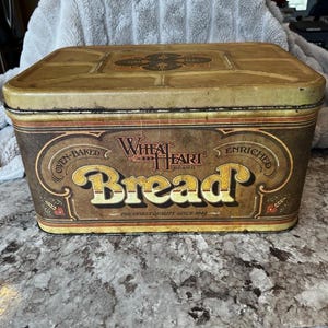 May include: Vintage rectangular bread box with a hinged lid. The box is primarily brown with gold lettering and accents. The text on the front reads "Wheat Heart Bread" and "The Finest Quality Since 1945".