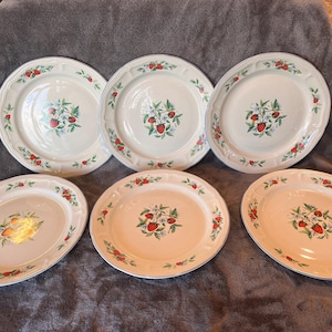 May include: A set of five round ceramic dinner plates featuring a white base with a scalloped edge. Each plate is decorated with a central cluster of red strawberries, green leaves, and small white flowers, with matching strawberry motifs along the rim.