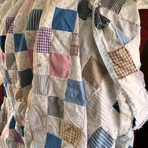 May include: A patchwork quilt with a variety of fabric patterns and colors. The quilt features squares of blue, pink, purple, and brown fabrics, with striped and checkered designs. The quilt is folded, showing its layered construction.