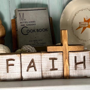 May include: Wooden blocks spelling out the word "FAITH" in white paint on a rustic wooden background. A wooden cross sits behind the blocks.