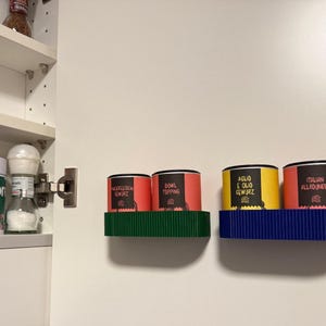 Könnte beinhalten: Ein weißer Küchenschrank mit einem Gewürzregal und einer Salzmühle. An der Wand befinden sich zwei Regale, eines grün und eines blau, die jeweils drei Gewürzbehälter mit deutschen und italienischen Etiketten halten.