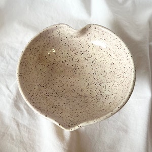 May include: A white heart-shaped ceramic bowl with a speckled brown glaze.